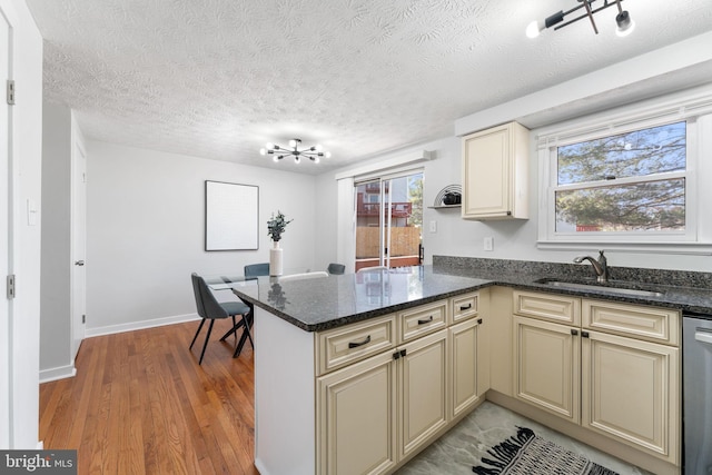 kitchen featuring a peninsula, cream cabinets, a sink, and light wood-style floors