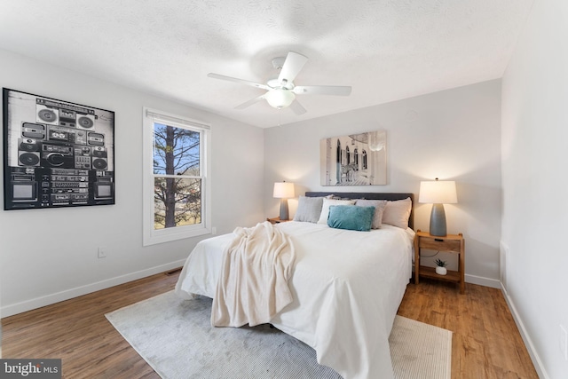 bedroom with a ceiling fan, a textured ceiling, baseboards, and wood finished floors