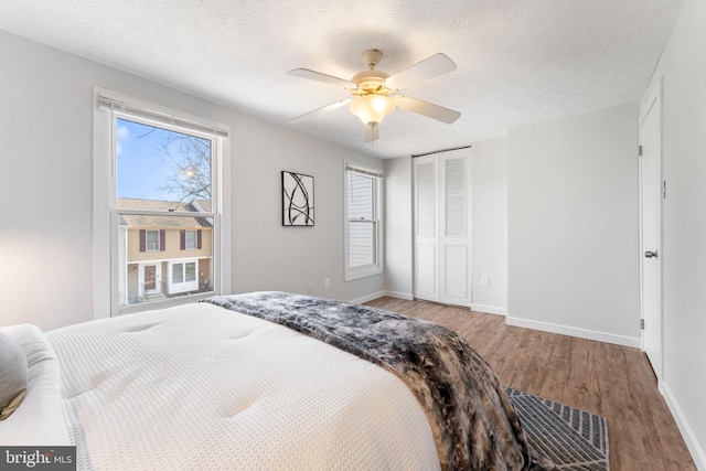 bedroom featuring a textured ceiling, a closet, wood finished floors, and baseboards