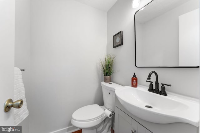 half bath with toilet, baseboards, and vanity