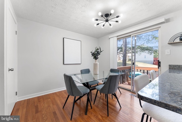 dining room with a notable chandelier, a textured ceiling, baseboards, and wood finished floors