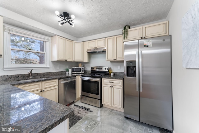 kitchen with under cabinet range hood, stainless steel appliances, a sink, marble finish floor, and cream cabinetry