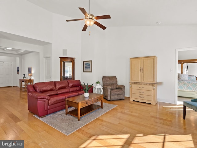 living area with ceiling fan, a high ceiling, visible vents, baseboards, and light wood-type flooring