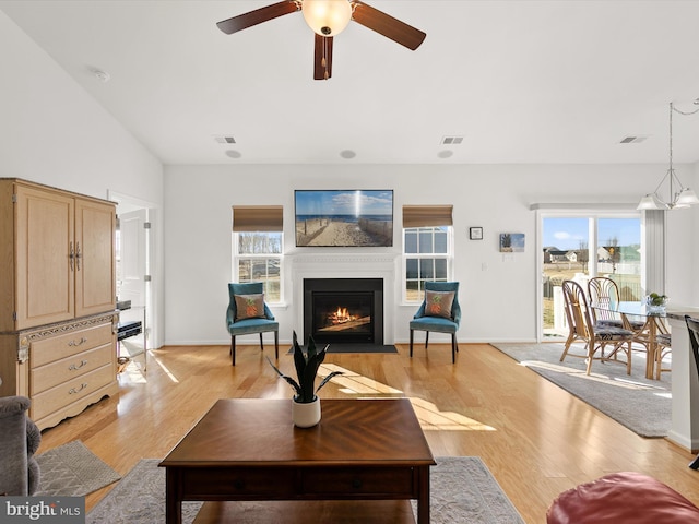 living room featuring light wood-type flooring, a fireplace with flush hearth, and visible vents