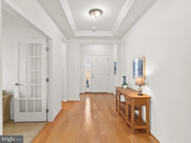 foyer featuring ornamental molding, light wood-type flooring, a raised ceiling, and baseboards