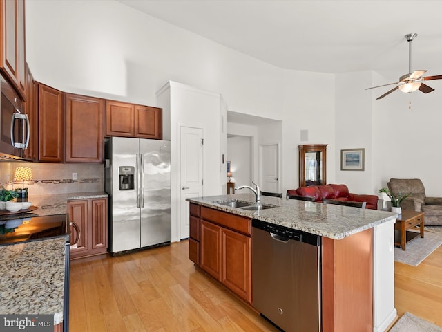 kitchen featuring a high ceiling, a sink, open floor plan, appliances with stainless steel finishes, and light wood finished floors