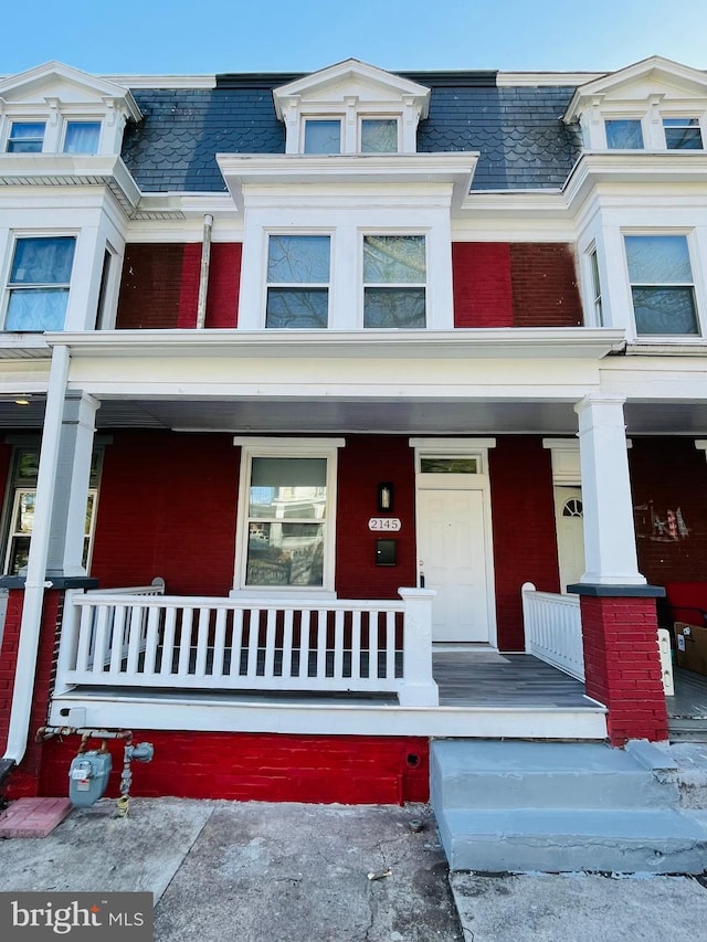 view of front of house with a porch, brick siding, and mansard roof