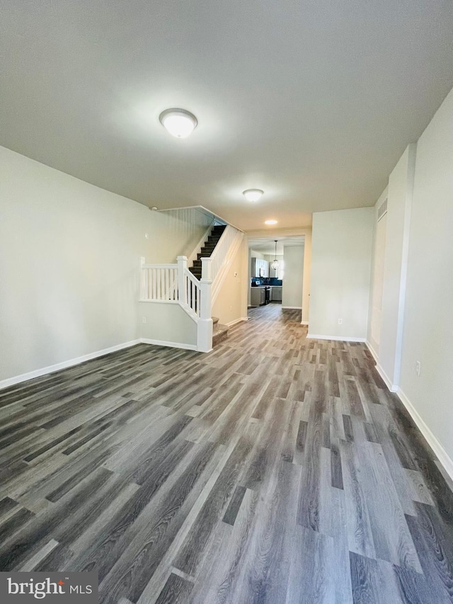 unfurnished living room with dark wood-type flooring, stairway, and baseboards