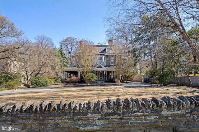 view of front facade featuring fence, covered porch, and a chimney