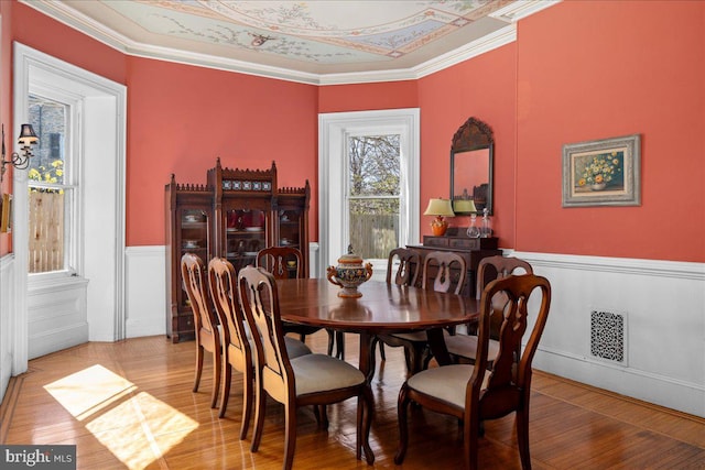 dining room featuring visible vents, wainscoting, light wood-type flooring, and crown molding