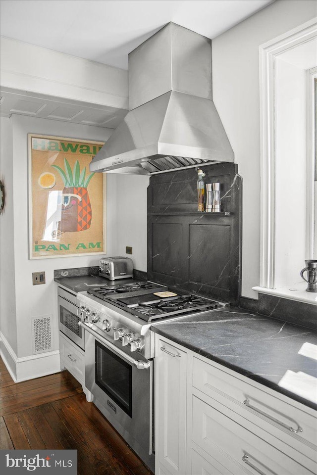 kitchen featuring dark countertops, high end stove, exhaust hood, dark wood-style floors, and white cabinetry