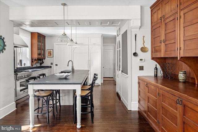 kitchen with a breakfast bar area, dark wood-style flooring, high end stainless steel range oven, dark countertops, and brown cabinets