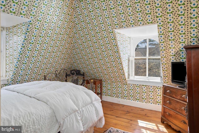 bedroom with hardwood / wood-style floors, baseboards, and wallpapered walls