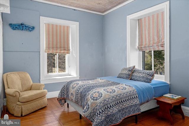 bedroom with multiple windows, baseboards, ornamental molding, and wood finished floors