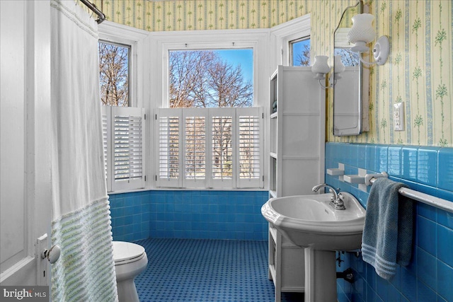 bathroom featuring toilet, tile walls, wainscoting, and wallpapered walls