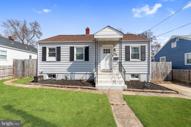 bungalow-style house with a shingled roof, a chimney, fence, and a front lawn