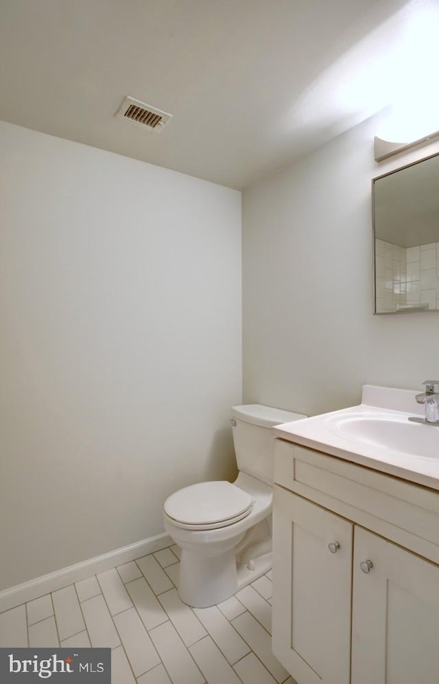 half bath featuring toilet, vanity, visible vents, and baseboards