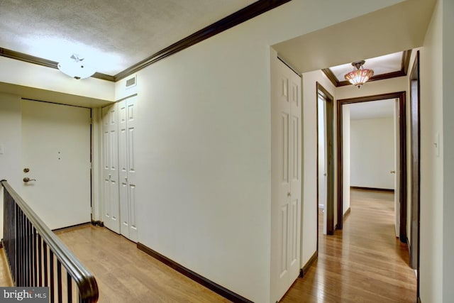 hallway featuring baseboards, light wood-type flooring, visible vents, and crown molding