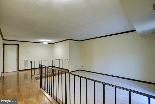 hallway featuring baseboards, visible vents, wood finished floors, and an upstairs landing