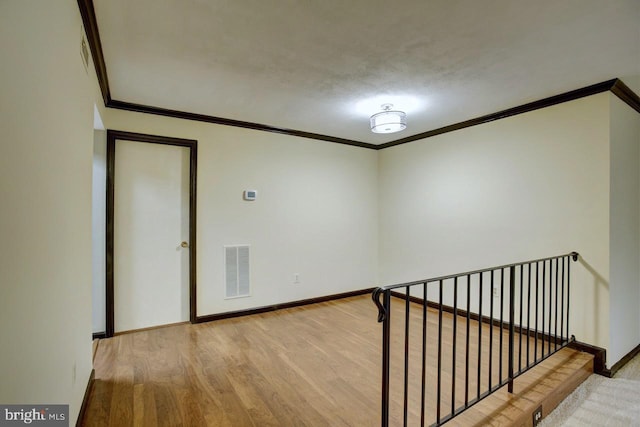 spare room featuring ornamental molding, visible vents, baseboards, and wood finished floors