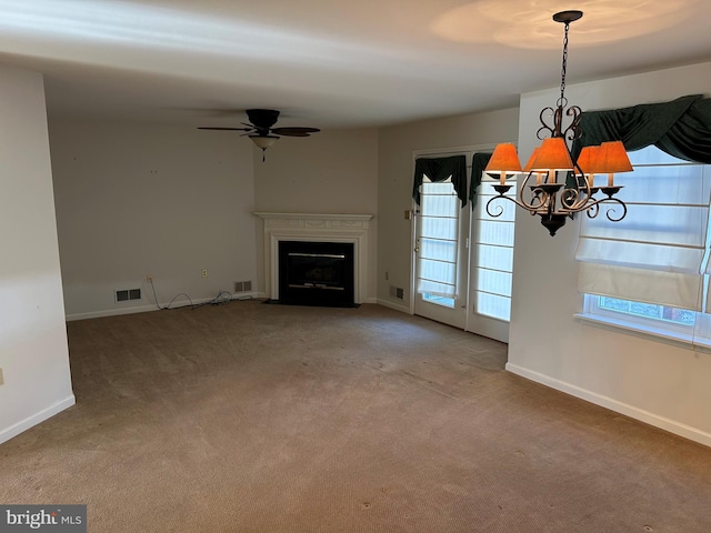 unfurnished living room featuring a wealth of natural light, visible vents, carpet, and ceiling fan with notable chandelier