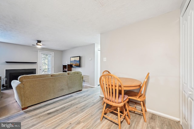 dining area featuring baseboards, visible vents, a fireplace, light wood-style floors, and a textured ceiling