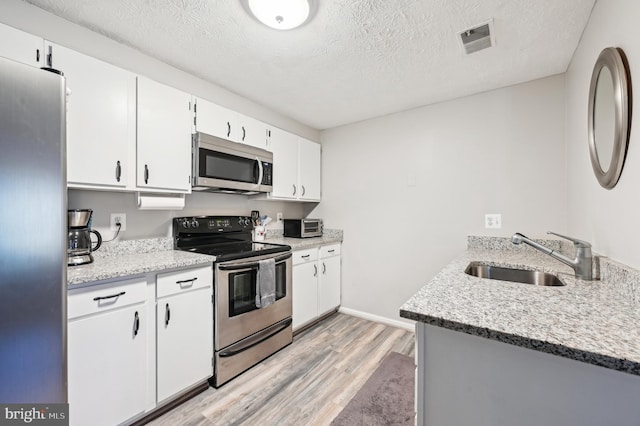 kitchen with light wood-type flooring, visible vents, a sink, stainless steel appliances, and white cabinets