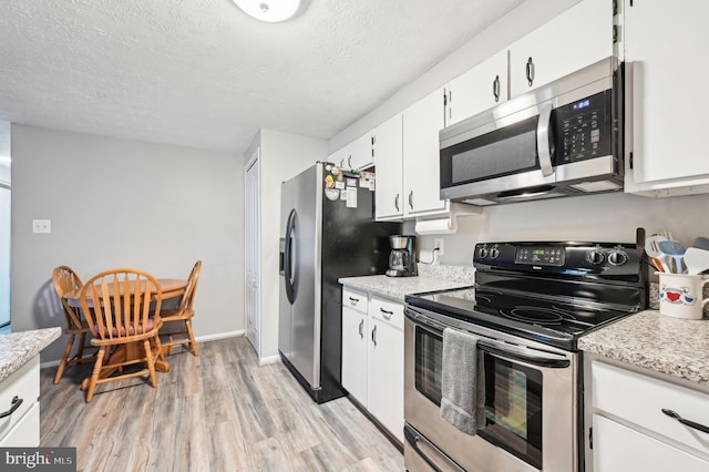 kitchen with a textured ceiling, stainless steel appliances, light wood-style floors, white cabinets, and baseboards