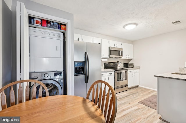 kitchen featuring stainless steel appliances, stacked washer and dryer, white cabinets, a textured ceiling, and light wood-type flooring