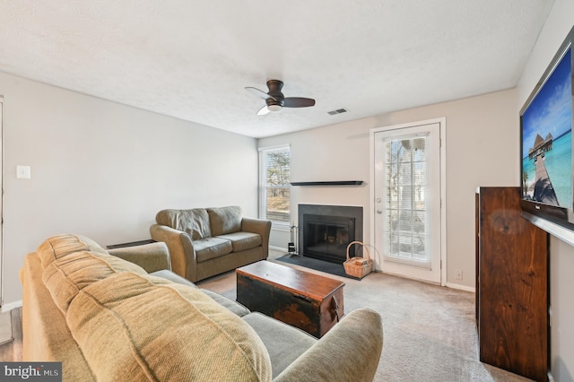 carpeted living room featuring visible vents, a fireplace with flush hearth, a textured ceiling, baseboards, and ceiling fan