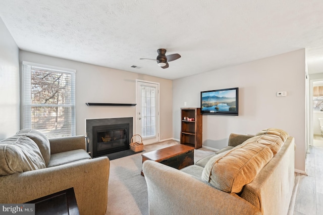 living room with visible vents, ceiling fan, baseboards, a fireplace with flush hearth, and a textured ceiling