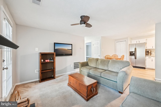 living area with visible vents, light colored carpet, a ceiling fan, and baseboards