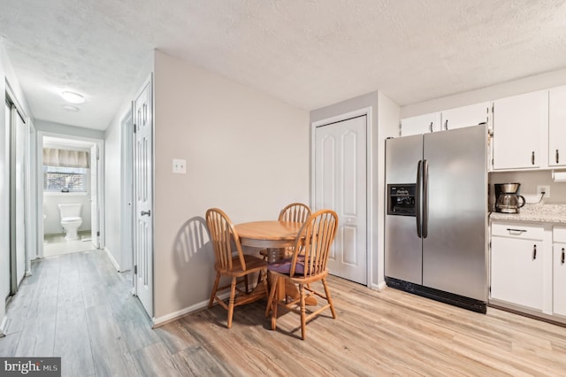 dining space featuring baseboards, a textured ceiling, and light wood-style flooring