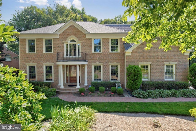 colonial house with brick siding, roof with shingles, and a balcony