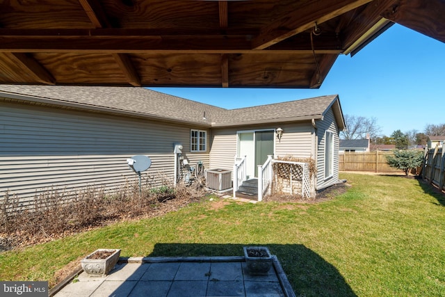 rear view of house featuring entry steps, central AC, a fenced backyard, a yard, and a shingled roof