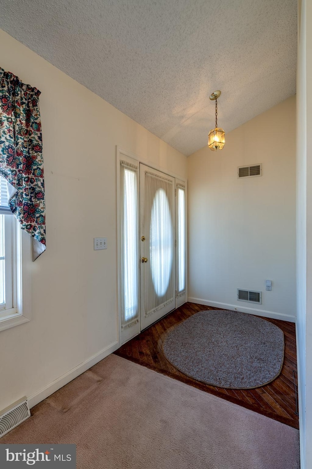 carpeted entrance foyer with visible vents, a textured ceiling, and lofted ceiling