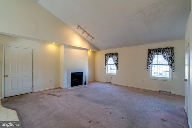 unfurnished living room with a tiled fireplace, track lighting, visible vents, and carpet floors