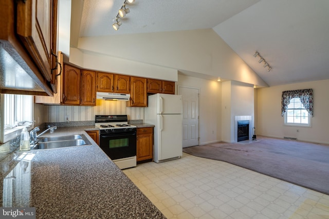 kitchen featuring a tiled fireplace, gas range, freestanding refrigerator, exhaust hood, and a sink