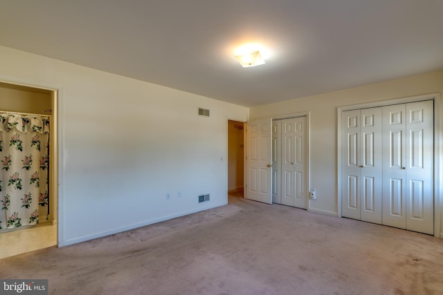 unfurnished bedroom featuring carpet flooring, visible vents, ensuite bathroom, and multiple closets