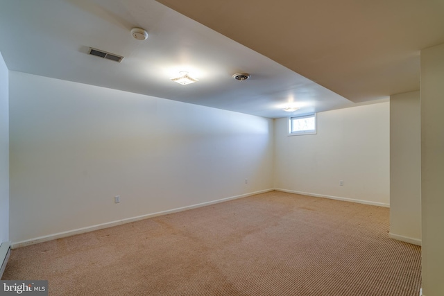 basement featuring a baseboard heating unit, visible vents, light colored carpet, and baseboards