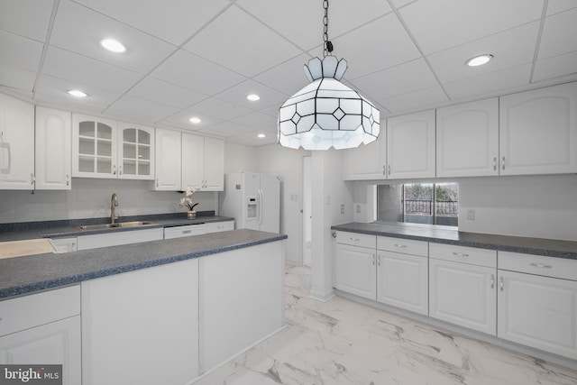 kitchen with a sink, white cabinets, white fridge with ice dispenser, dark countertops, and glass insert cabinets