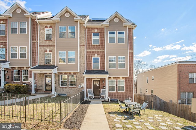 townhome / multi-family property with fence private yard, brick siding, and solar panels