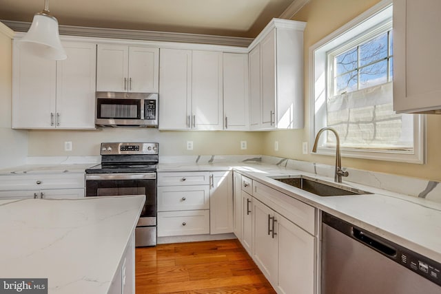 kitchen with pendant lighting, stainless steel appliances, light wood-style flooring, white cabinets, and a sink