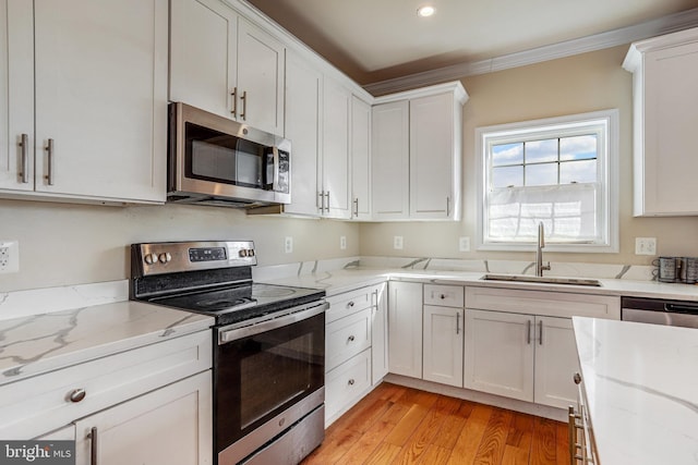 kitchen with light wood finished floors, appliances with stainless steel finishes, ornamental molding, white cabinets, and a sink