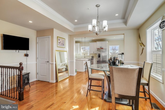 dining area featuring a chandelier, visible vents, a tray ceiling, light wood finished floors, and crown molding