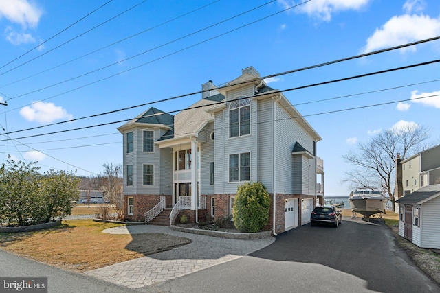 view of front facade with driveway, a garage, a chimney, and brick siding