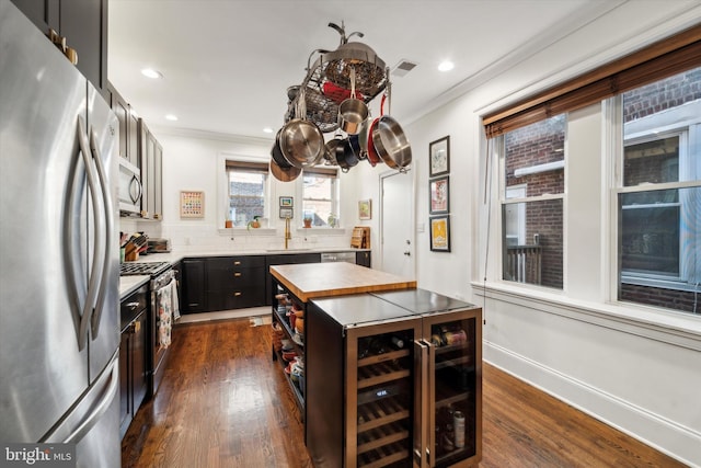 kitchen featuring wine cooler, appliances with stainless steel finishes, dark cabinetry, and crown molding