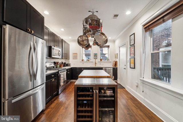 kitchen with dark cabinetry, beverage cooler, appliances with stainless steel finishes, crown molding, and tasteful backsplash