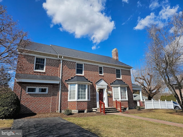 view of front of house featuring a front yard, fence, brick siding, and a chimney