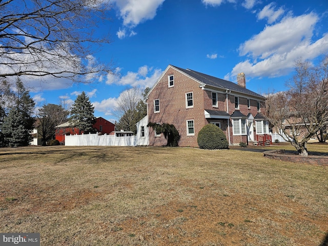 view of home's exterior featuring a yard, brick siding, a chimney, and fence